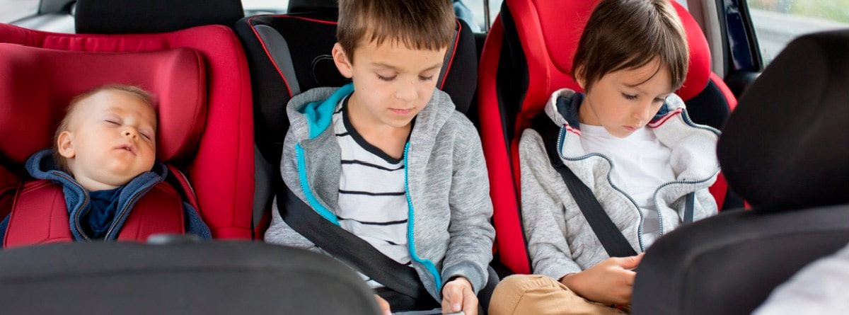 tres niños en sillas infantiles en los asientos traseros del coche