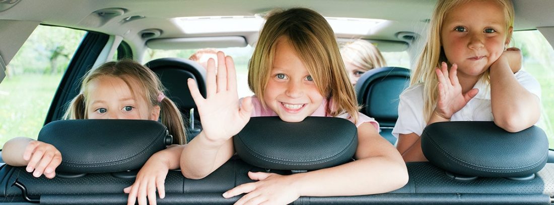 Tres niñas saludando desde los asientos traseros de un coche