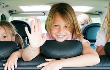 Tres niñas saludando desde los asientos traseros de un coche