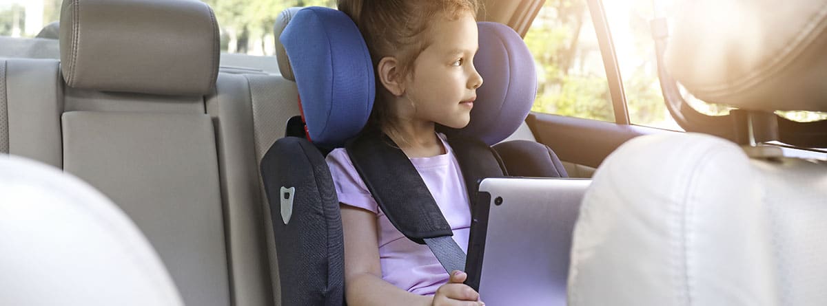 una niña mirando por la ventana del coche, sentada en una silla infantil