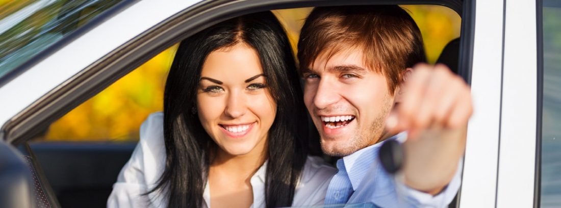 Hombre y mujer sonrientes dentro de un coche mostrando las llaves