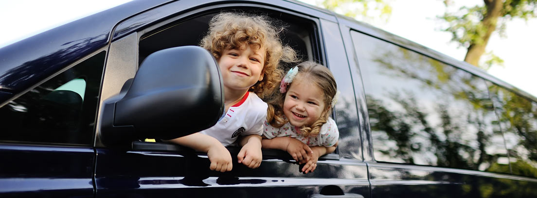 Dos niños sonrientes asomados por la ventanilla de un monovolumen por menos de 20.000 euros