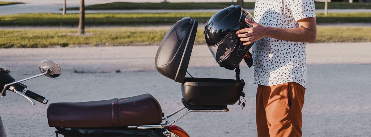 chico guardando un casco en el baúl de la moto