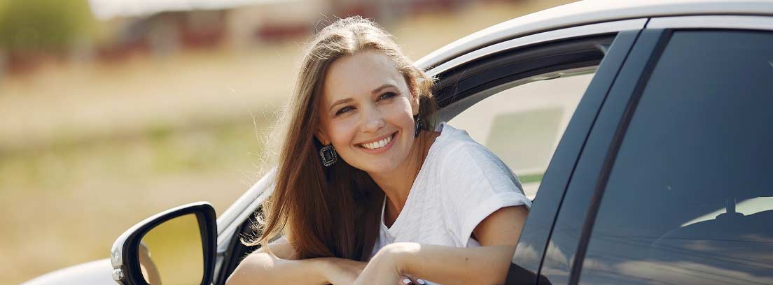 Mujer sonriente asomada por la ventanilla del conductor de un coche