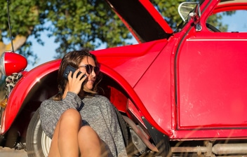 Mujer hablando por teléfono junto a un coche antiguo con el capó abierto