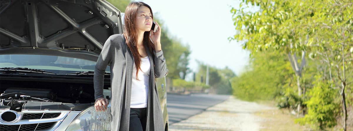 Mujer llamando por teléfono junto a un coche con el capó abierto