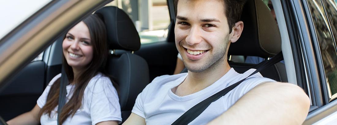 Hombre joven sonríe sentado al volante de un vehículo al lado mujer joven.