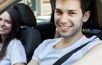 Hombre joven sonríe sentado al volante de un vehículo al lado mujer joven.