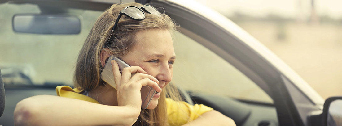 Mujer sentada dentro de coche y apoyada en ventana con teléfono sobre su oreja.