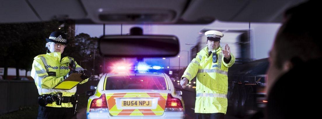 pareja de policias al lado de un coche patrulla con las luces encendidas