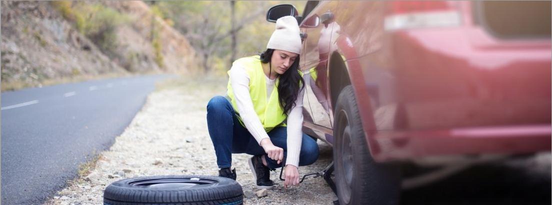 Mujer cambiando la rueda de su coche en la carretera
