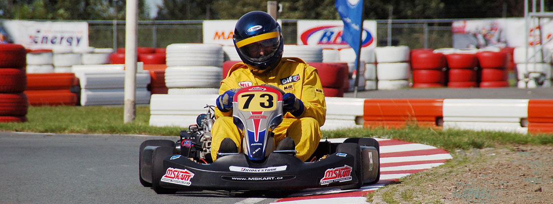 Piloto con mono amarillo y casco negro en un kart con número 73.