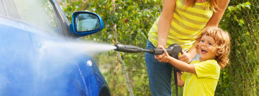 Niño con una manguera de agua a presión lavando el coche junto a una mujer