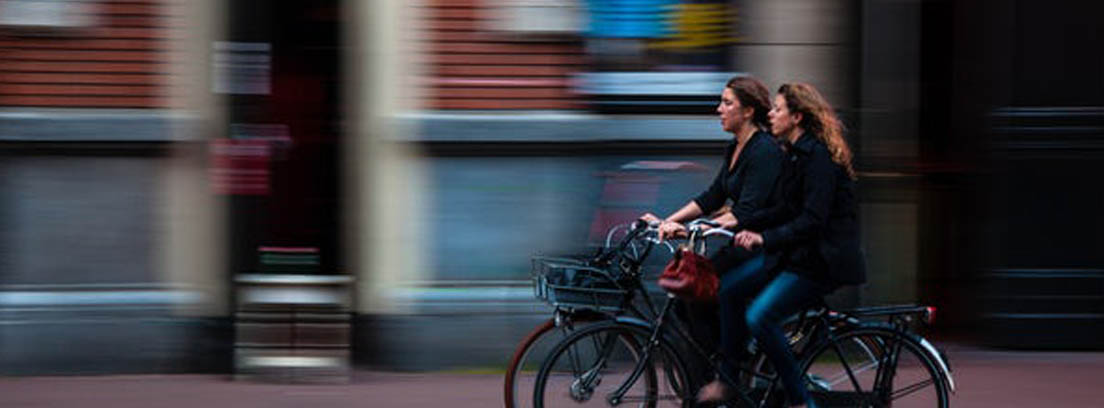 Dos mujeres en bicicleta por una calle urbana