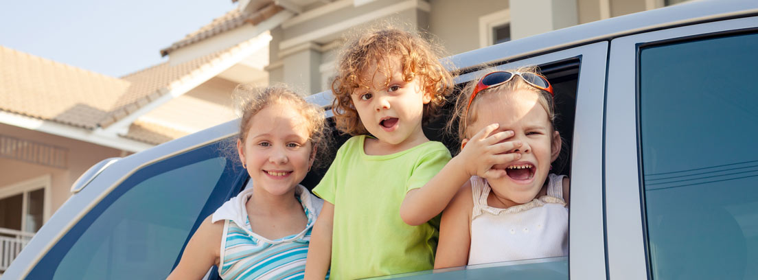 Tres niños felices asomados por la ventanilla de un coche
