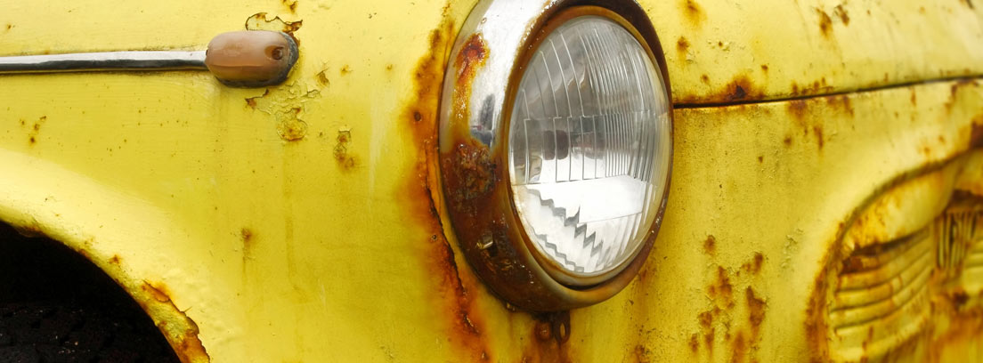 Primer plano del faro de un coche amarillo con la carrocería oxidada
