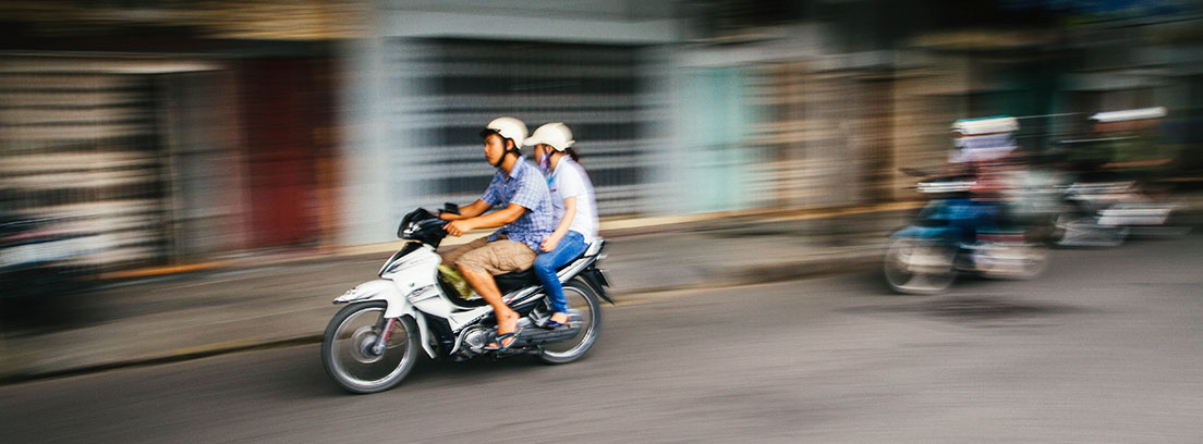 Dos personas subidas en una moto circulando por ciudad