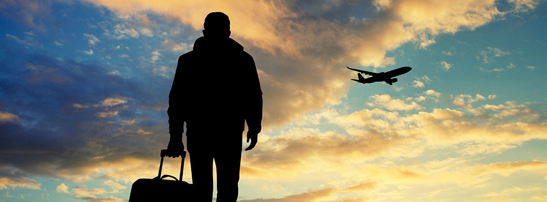 Hombre andando con una maleta y un avión volando en un atardecer