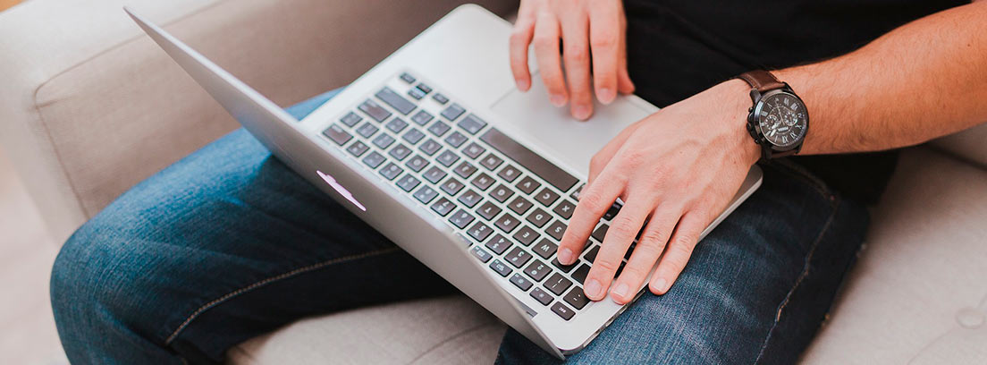 Ordenador portátil sobre rodillas de persona con manos sobre teclado