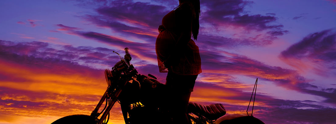 Mujer embaraza sobre una moto al atardecer