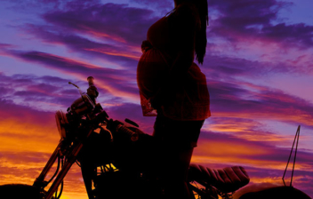 Mujer embaraza sobre una moto al atardecer