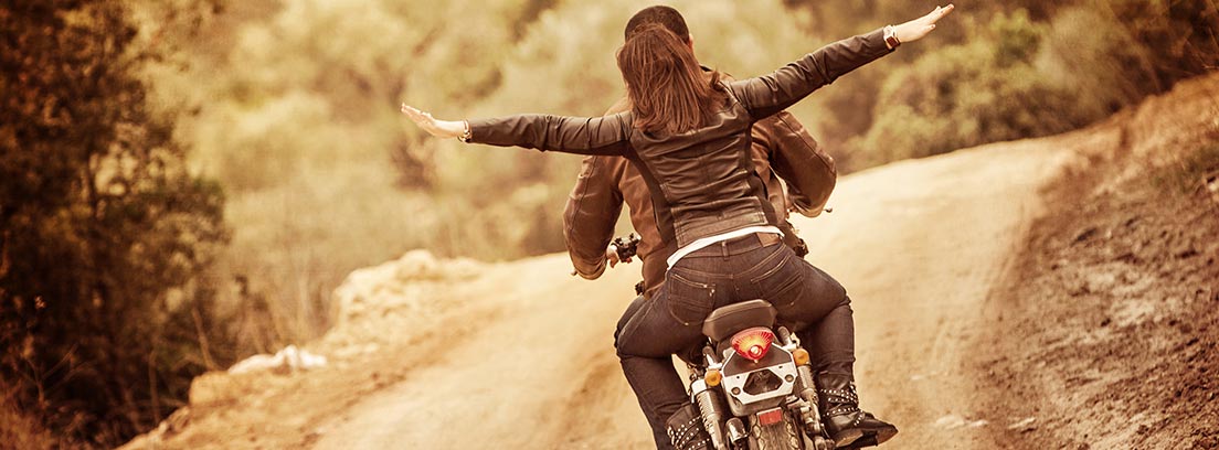 Hombre y mujer de espaldas circulando por una carretera con una moto
