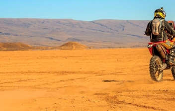 Piloto de espaldas circulando con su moto por el desierto