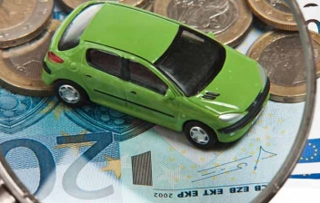 Lupa sobre un coche de juguete verde y billetes y monedas de euro