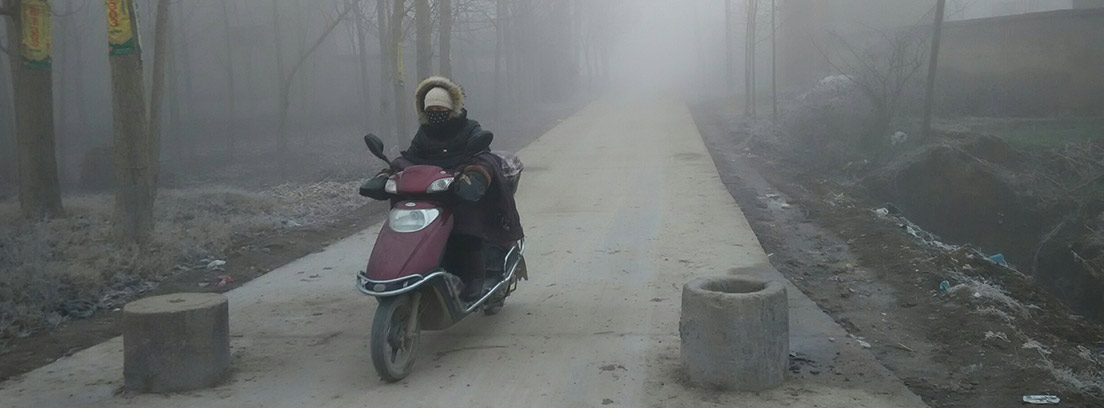 Hombre abrigado circulando con una moto en la niebla