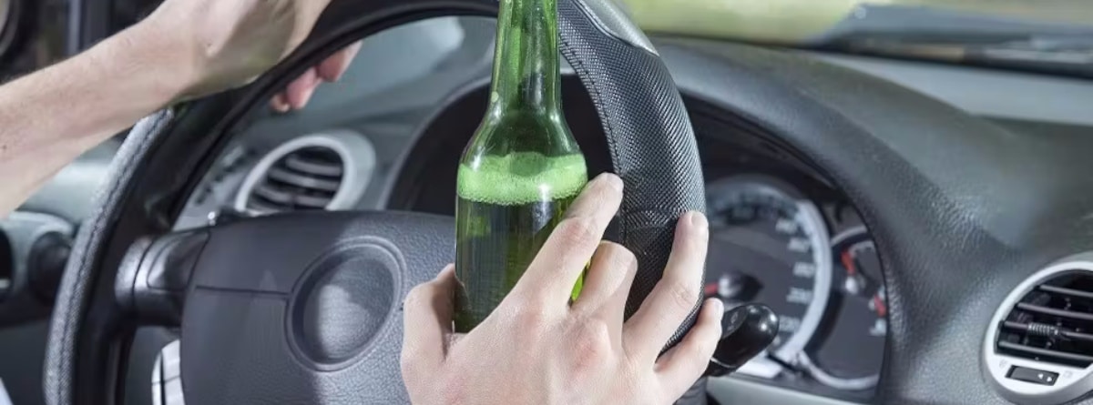Persona conduciendo con una botella en la mano
