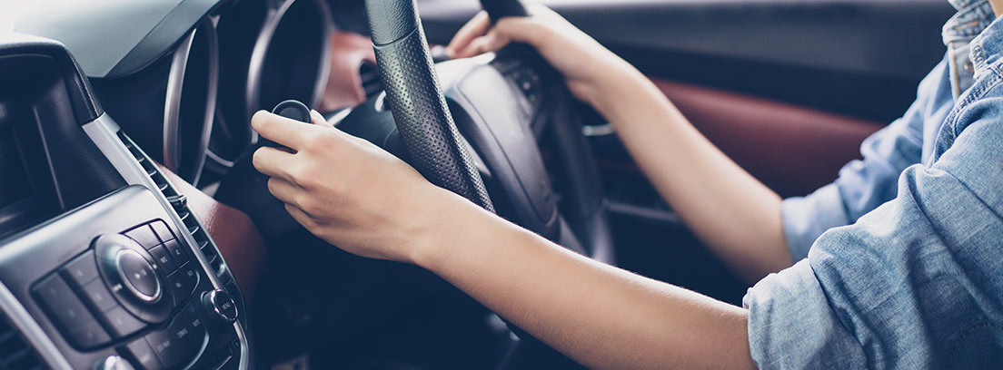 Interior de un coche con una mujer con las manos en el volante conduciendo a la derecha