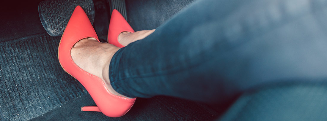 Pies con zapatos de tacón rojo sobre pedales de un vehículo.
