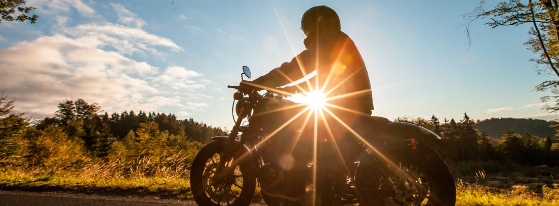Moto y motorista de perfil en una carretera de montaña con el sol al fondo