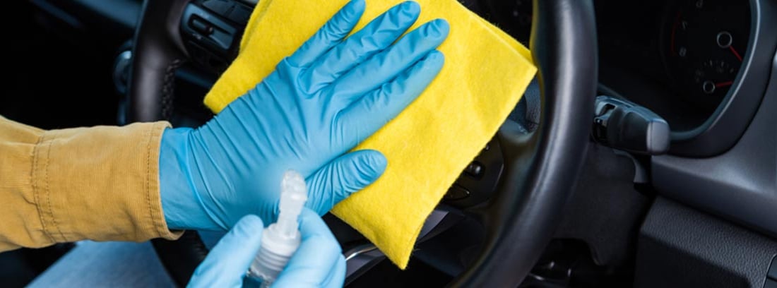 Manos con guantes limpiando el interior de un coche