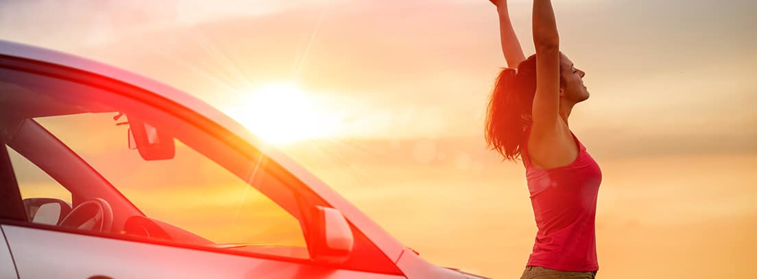 Mujer con los brazos en alto en una puesta de sol junto a un coche