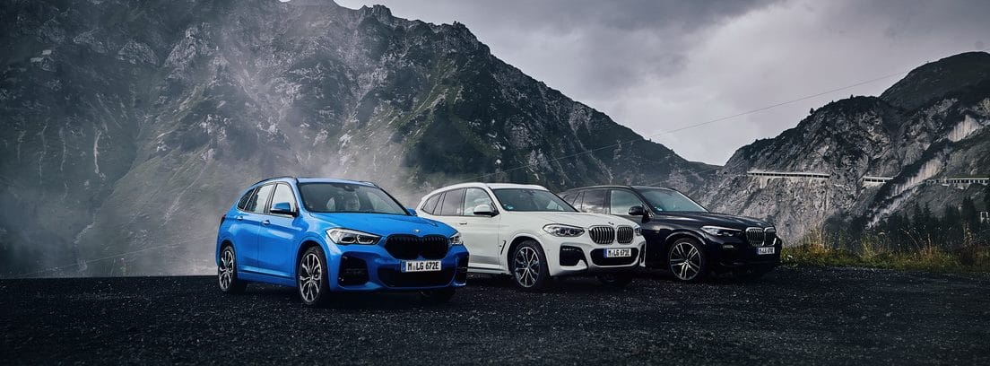 Tres coches BMW X1 xDrive25e en colores azul, blanco y negro parados entre montañas