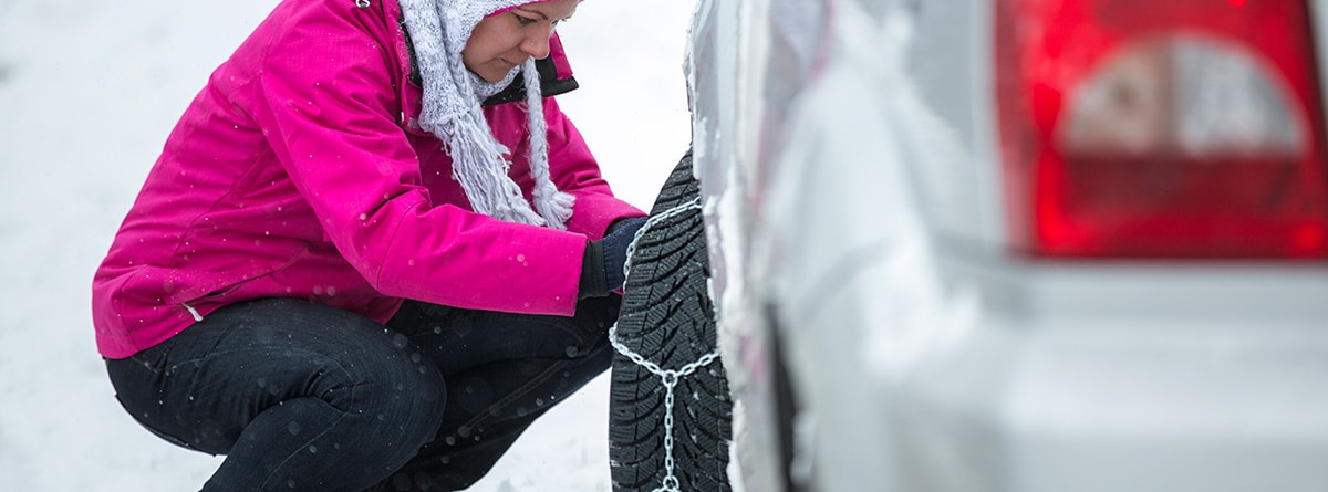 Mujer abrigada colocando cadenas en un coche en la nieve