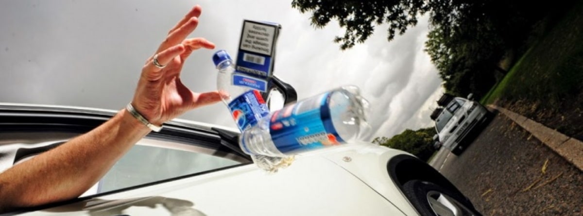 persona tirando botellas de plástico y paquete de tabaco por la ventana del coche