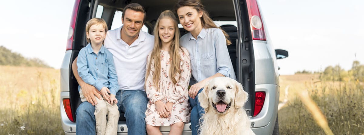Familia sonriente con perro en el maletero de un furgoneta