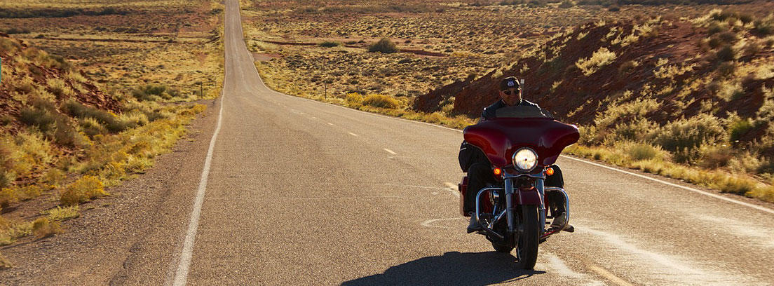 Hombre conduciendo moto por una larga carretera vacía.