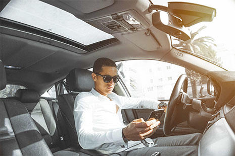 chico dentro del coche con gafas de sol mirando el smartphone