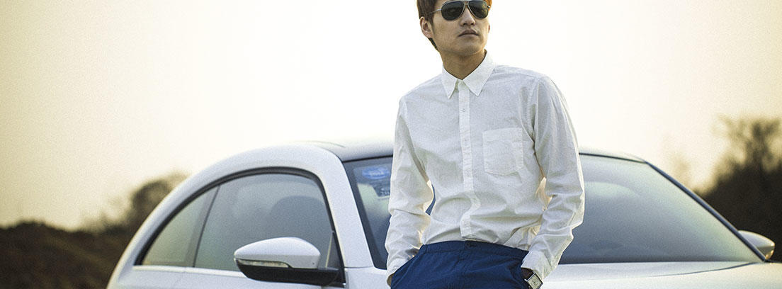 Hombre con gafas de sol y camisa blanca apoyado coche blanco Volkswagen escarabajo.