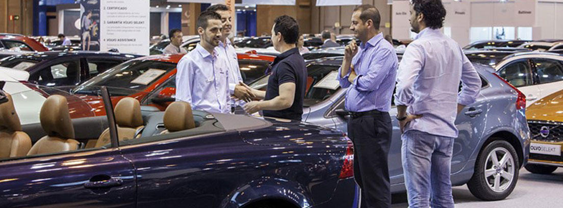 Coche descapotable azul oscuro con varias personas al lado y otros coches
