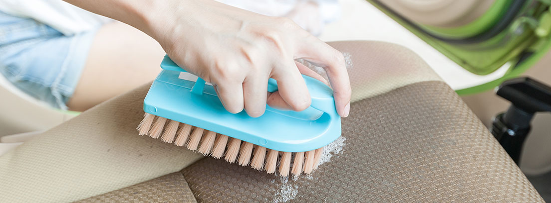 Tapicería de piel o de tela para el coche y su mantenimiento y limpieza Limpiar con un cepillo azul las manchas de la tapicería de tela de un coche de color gris.
