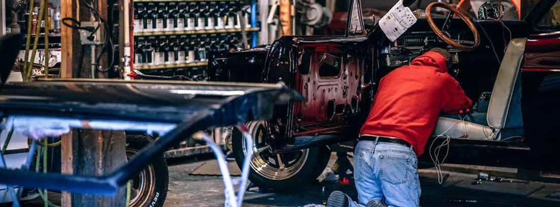 Persona arrodillada dentro de coche con piezas y herramientas alrededor