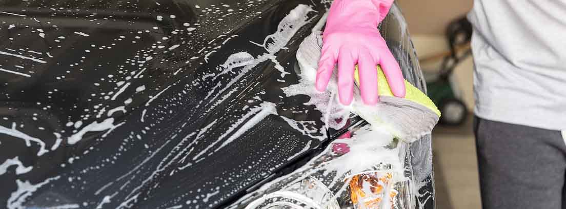Mano con guante rosa sujeta esponja amarilla sobre exterior de coche con espuma