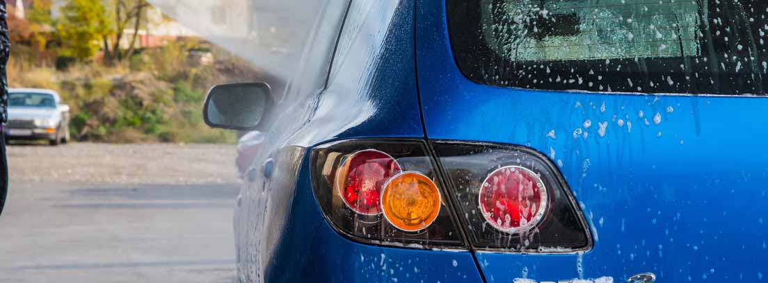 Vista de la parte trasera de un automóvil azul y una manguera de lavado a presión para el coche