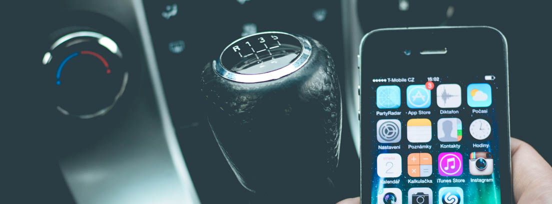 mano sujetando un teléfono móvil al lado de la palanca de cambios de un coche