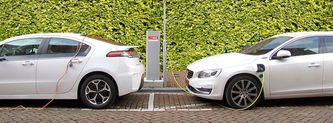 : Dos coches eléctricos enchufados a un punto de carga