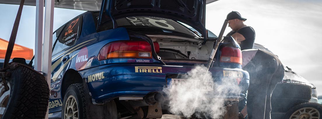 Coche azul elevado por gato y echando humo por tubo de escape.